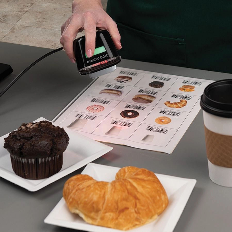 Datalogic Magellan 1500i black USB presentation scanner reading 1D/2D bakery barcodes at a POS checkout counter